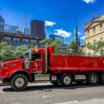 a red dump truck driving down a street next to tall buildings