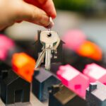 Hand holding house keys over miniature houses
