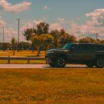 Dark suv drives along a grassy roadside.